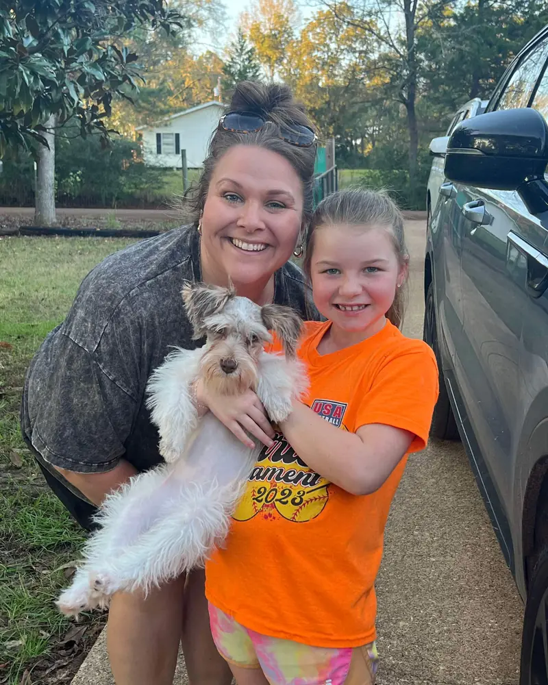 A woman and a young girl leaning together over the new white-and-grey puppy they are holding between them.