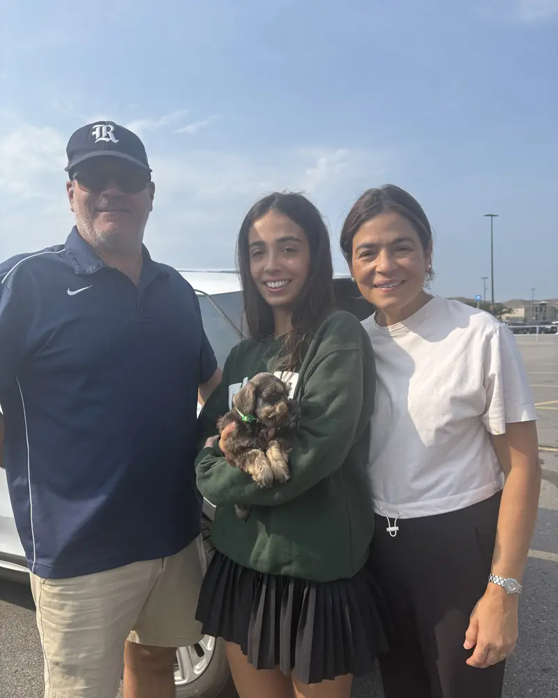 A man, a teenager and a woman in a car park, the teenager holding their new brown puppy in both arms.