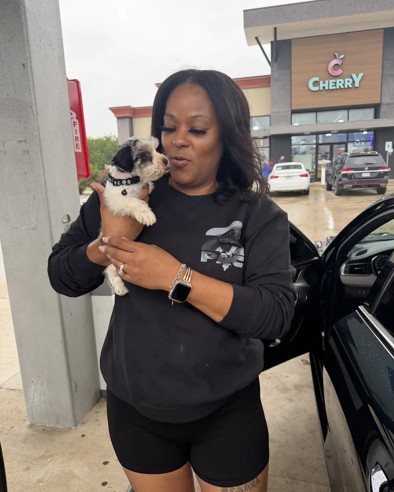 A woman leaning in to the new black-and-white puppy in her arms under a filling-station canopy.