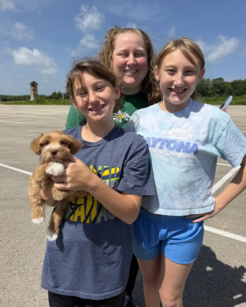 A woman and two children in a wide, empty car park, one of the children holding their new tan puppy.