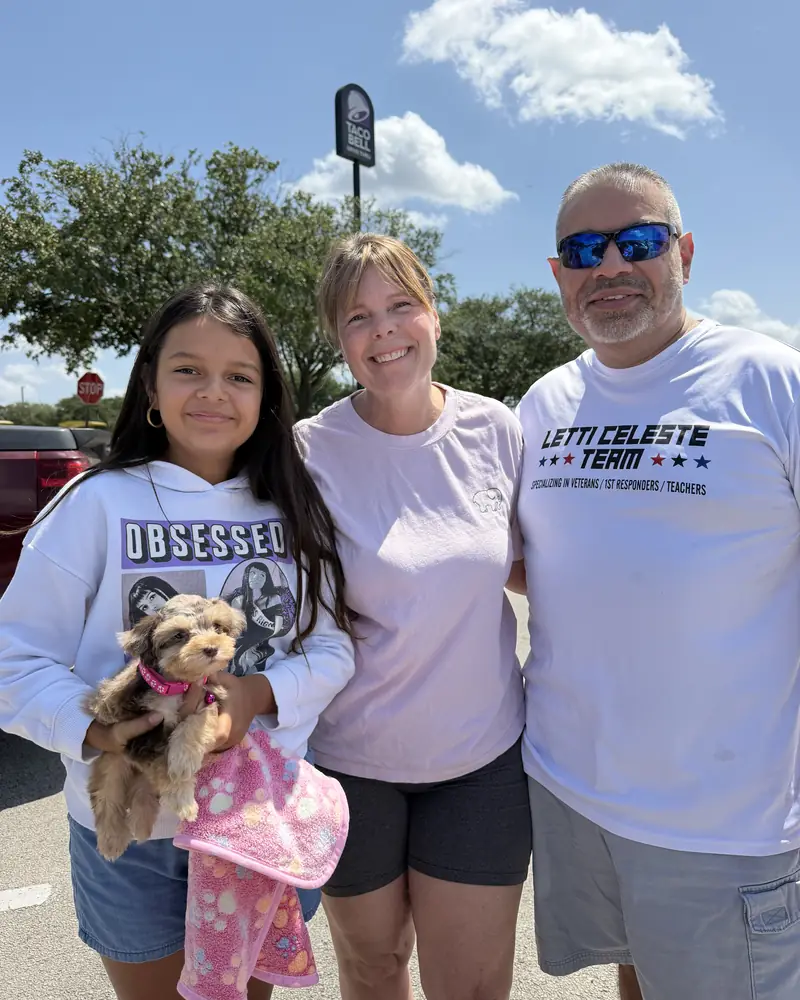 A man, a woman and a girl standing together, the girl holding their new tan puppy in a pink blanket.