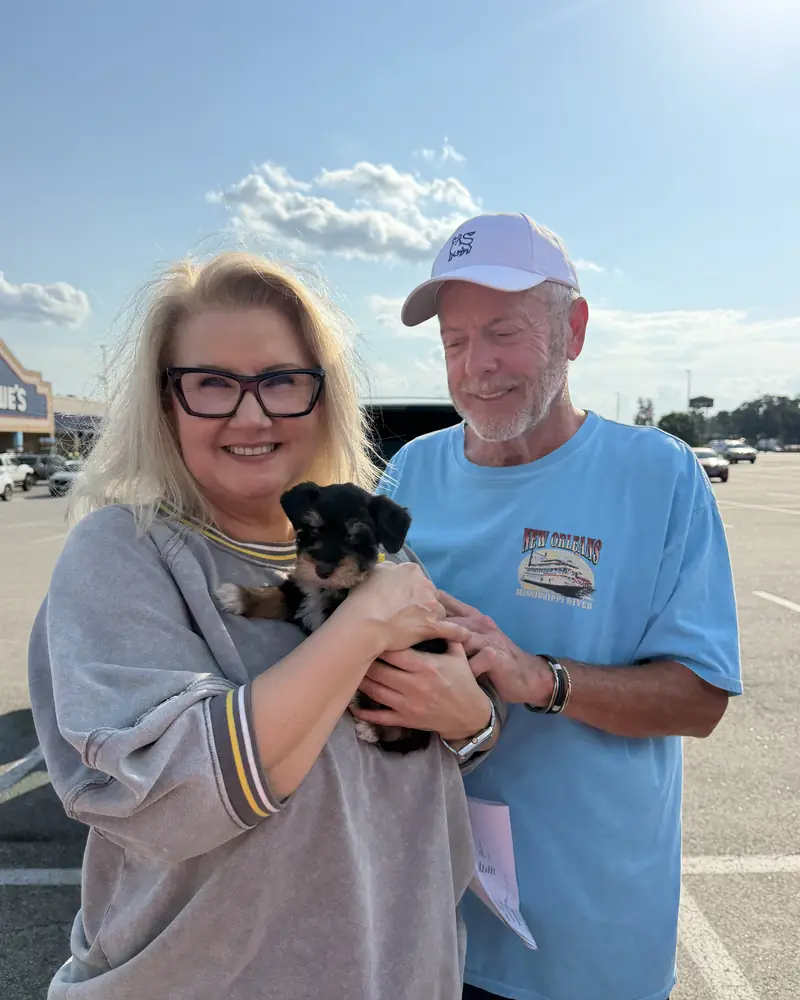 A couple in a car park, the woman holding their new black-and-tan puppy while the man steadies it.